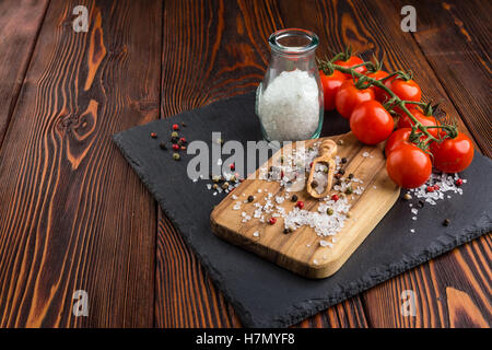 Cherry tomatoes, salt in glass jar, sprinkled with salt and pepper, olive wood spoon on cutting board Stock Photo