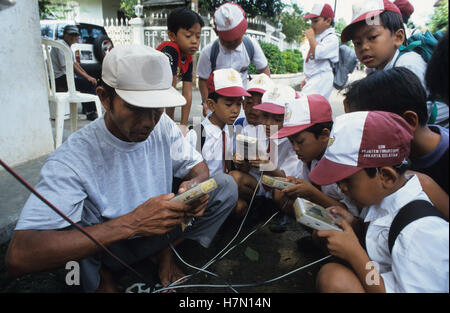 INDONESIA Java, Jakarta, kids playing Nintendo game boy games at street vendor, Game Boy is an 8-Bit handheld gaming console, developed by Gunpei Yokoi Stock Photo
