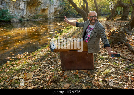 Concept of happy man sitting on vintage suitcase and playing with his smartphone Stock Photo