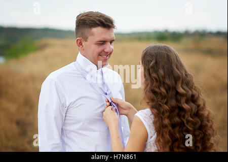 bride dress for groom his tie on the nature in field Stock Photo