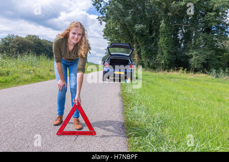 European woman placing hazard warning triangle on rural road Stock Photo