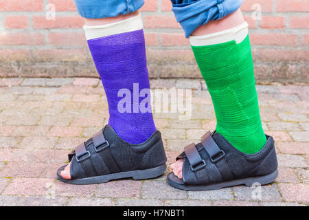 Standing teenage boy with two colored gypsum legs outside Stock Photo