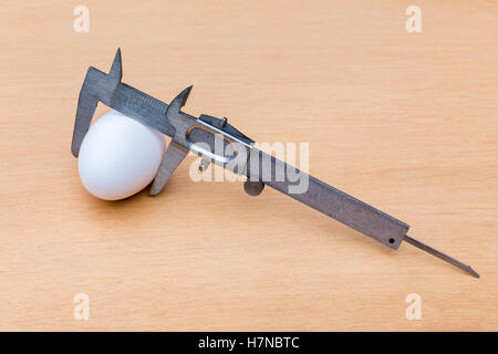 Vernier caliper measuring white chicken egg on wood Stock Photo