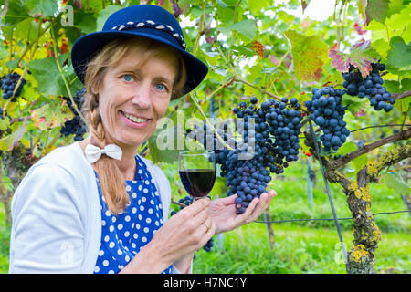 Woman in vineyard showing blue bunches of grapes and red wine Stock Photo