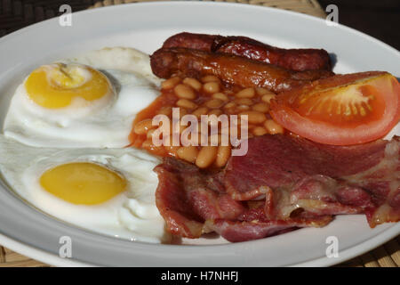 English breakfast served by a hotel in Malta - two fried eggs, rashers of local bacon, two sausages, tomato, baked beans. Stock Photo