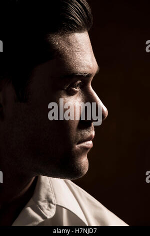 Handsome young man with stubble in serious head and shoulders studio portrait with amber tones and dramatic lighting in profile. Stock Photo