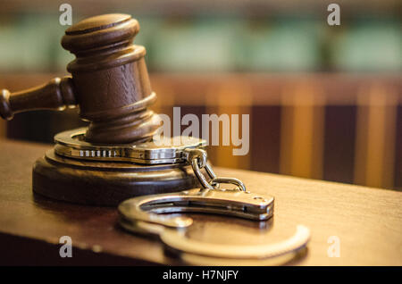 close up of gavel and handcuffs on judge's bench in courtroom with jury box and seats in the background Stock Photo