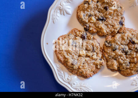 Three homemade oatmeal raisin cookies with walnuts on a white plate, blue background. Closeup. USA Stock Photo