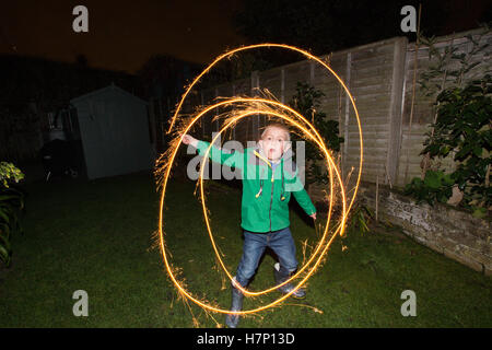 Boy (aged 5) in suburban backgarden with hand-held firework type 'sparkler' on Bonfire night or traditionally Guy Fawkes night. Stock Photo