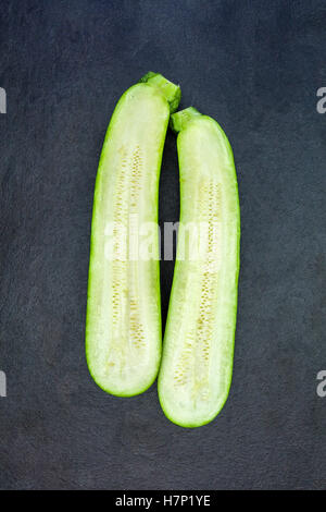 Two halves of fresh green zucchini isolated on dark gray slate stone background Stock Photo