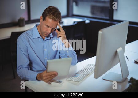 Thoughtful businessman using digital tablet and desktop pc Stock Photo
