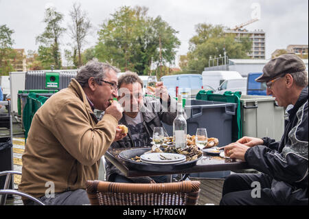 Three men eating oysters and drinking white wine in the rain, Salon des Vins wine fair, Toulouse, Haute-Garonne, Occitanie, France outdoor dish Stock Photo