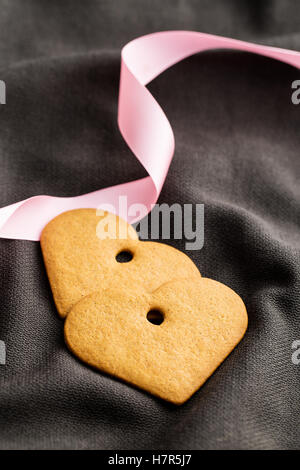 Two gingerbread hearts with pink ribbon on brown fabric. Stock Photo