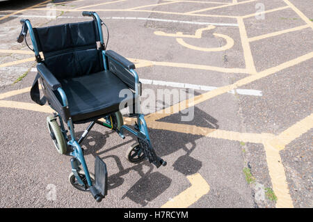 An empty wheelchair next to disabled parking bays in a car park.