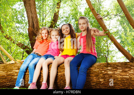 Four cute girl friends sitting on fallen tree Stock Photo