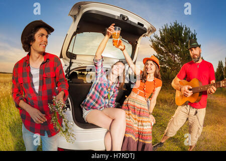 Happy girls cheering with beer sitting in car boot Stock Photo