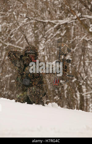 Male Bowhunter Draws Bow In Snow While Deer Hunting Stock Photo