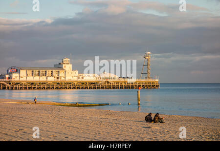 A couple sit alone on the beach enjoying the calm sea and evening sunlight with the pier in the background at Bournemouth, UK Stock Photo
