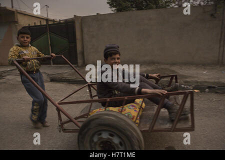 Qayyarah, Niniveh, Iraq. 8th Nov, 2016. 08/11/2016. Qayyarah, Iraq. Two boys smile as they play with a handcart in the smoke filled city of Qayyarah, Iraq. Oil wells in and around the town of Qayyarah, Iraq, we set alight in July 2016 by Islamic State extremists as the Iraqi military began an offensive to liberated the town.For two months the residents of the town have lived under an almost constant smoke cloud, the only respite coming when the wind changes. Credit:  ZUMA Press, Inc./Alamy Live News Stock Photo