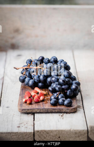 Bunch of ripe blue grapes and wild strawberries on a light wooden background. Fresh autumn fruits. Light food photography. Stock Photo