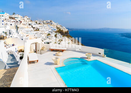 View of caldera and luxury swimming pool in foreground, typical white architecture of Imerovigli village on Santorini island, Greece. Stock Photo