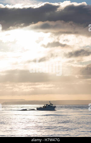 A boat at sea during sunrise sunset with stormy dark clouds on a calm sea. Stock Photo