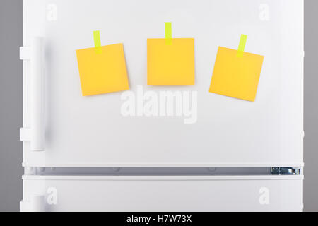 Three blank yellow paper notes attached with yellow stickers on white refrigerator door Stock Photo