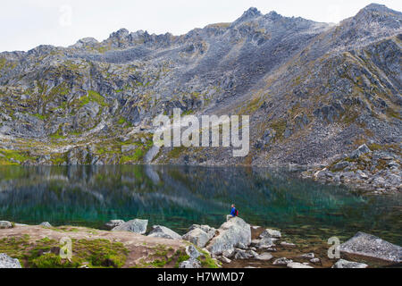 Hiker sitting on a boulder and overlooking Gold Cord Lake in Hatcher Pass, Southcentral Alaska, USA Stock Photo