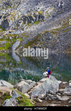 Hikers sitting on a boulder and overlooking Gold Cord Lake in Hatcher Pass, Southcentral Alaska, USA Stock Photo