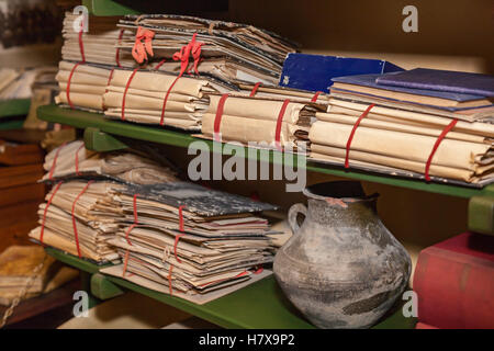 Volumes of documents. Volumes of document cases tied with red ribbons, folded on the shelves with books and crock. Stock Photo