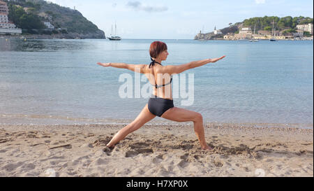 A woman practicing yoga on a beach in Majorca. Warrior pose shown. Stock Photo