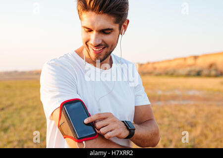 Smiling young sportsman using blank screen mobile phone on armband outdoors Stock Photo