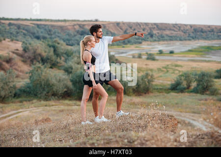 Young beautiful fitness couple standing on a hill and looking at something Stock Photo