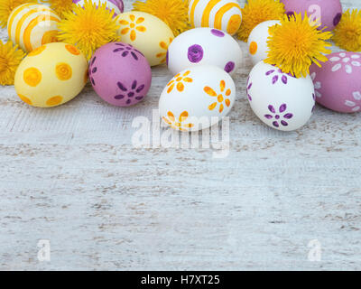 White, violet and yellow easter eggs decorated by stripes, dots and flowers and dandelions on the white wooden board Stock Photo