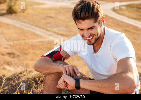 Handsome young sportsman sitting and using smart watch outdoors Stock Photo