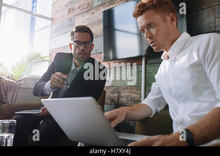 Two young man sitting in office and discussing business using laptop. Business colleagues working on laptop during meeting. Stock Photo