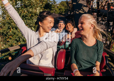 Shot of young friends enjoying and cheering on roller coaster ride. Young people having fun on rollercoaster at amusement park. Stock Photo