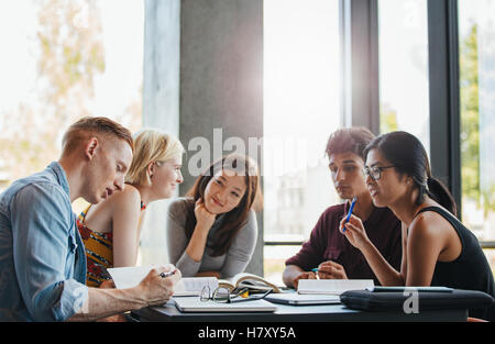Group of students doing school assignment in library. Multiethnic young people reading reference books for study. Stock Photo