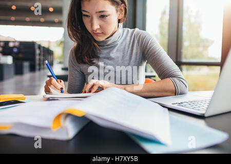 Close up image of a young female student doing assignments in library. Asian woman taking notes from textbook. Stock Photo