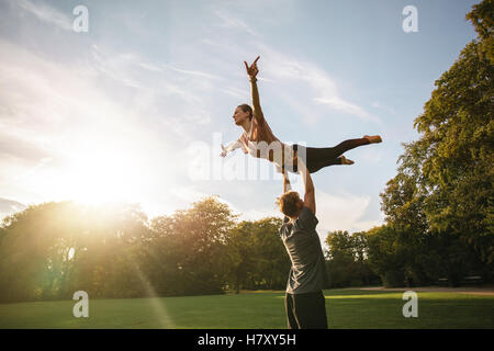 Strong young couple doing acroyoga outdoors. Man and woman in park practicing pair yoga. Stock Photo