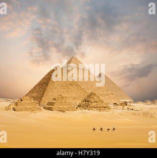 Dramatic sunset behind all distant Egyptian Pyramids together with line of camels walking in foreground in Giza, Cairo, Egypt. Stock Photo