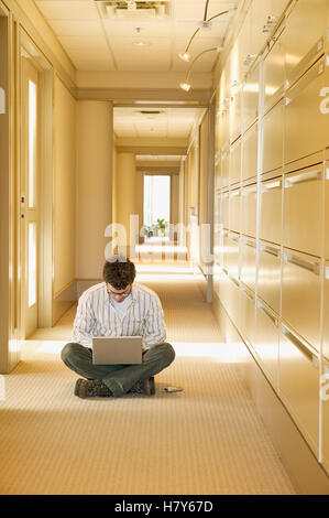 man sitting in hallway working on laptop computer Stock Photo