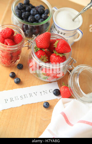 Strawberries, raspberries and blueberries in glass jars with the word preserving on cutting board Stock Photo