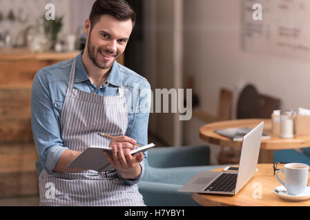 Joyful young man smiling and making notes. Stock Photo