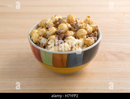 A colorful bowl filled with gourmet popcorn, almonds and pecans on a wood table. Stock Photo