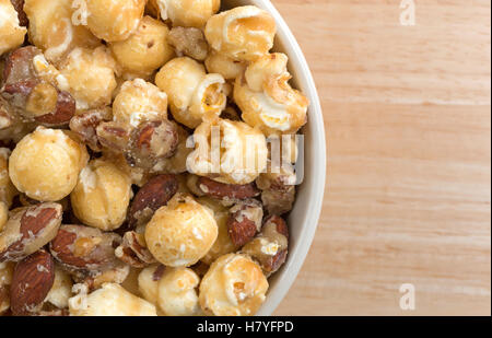 Top close view of a bowl filled with gourmet popcorn, almonds and pecans on a wood table. Stock Photo