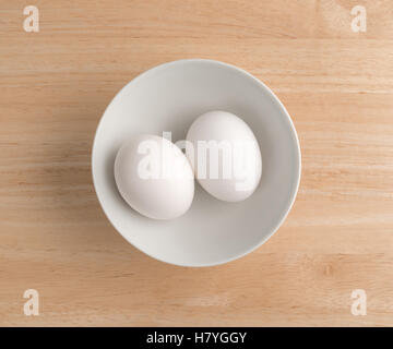 Top view of two eggs in a white bowl on a wood table. Stock Photo
