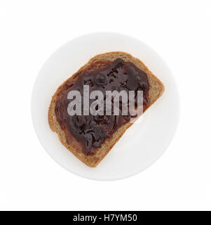 Top view of plum preserves spread on a piece of wheat bread on a plate isolated on a white background. Stock Photo