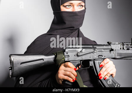 Muslim woman with a machine gun. An armed woman shoots. Islamic Woman holding an automatic weapon. Concept of war and terrorism Stock Photo
