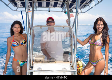 Two young women posing with male captain on small fishing boat. Banderas Bay - Pacific Ocean, Puerto Vallarta, Mexico Stock Photo